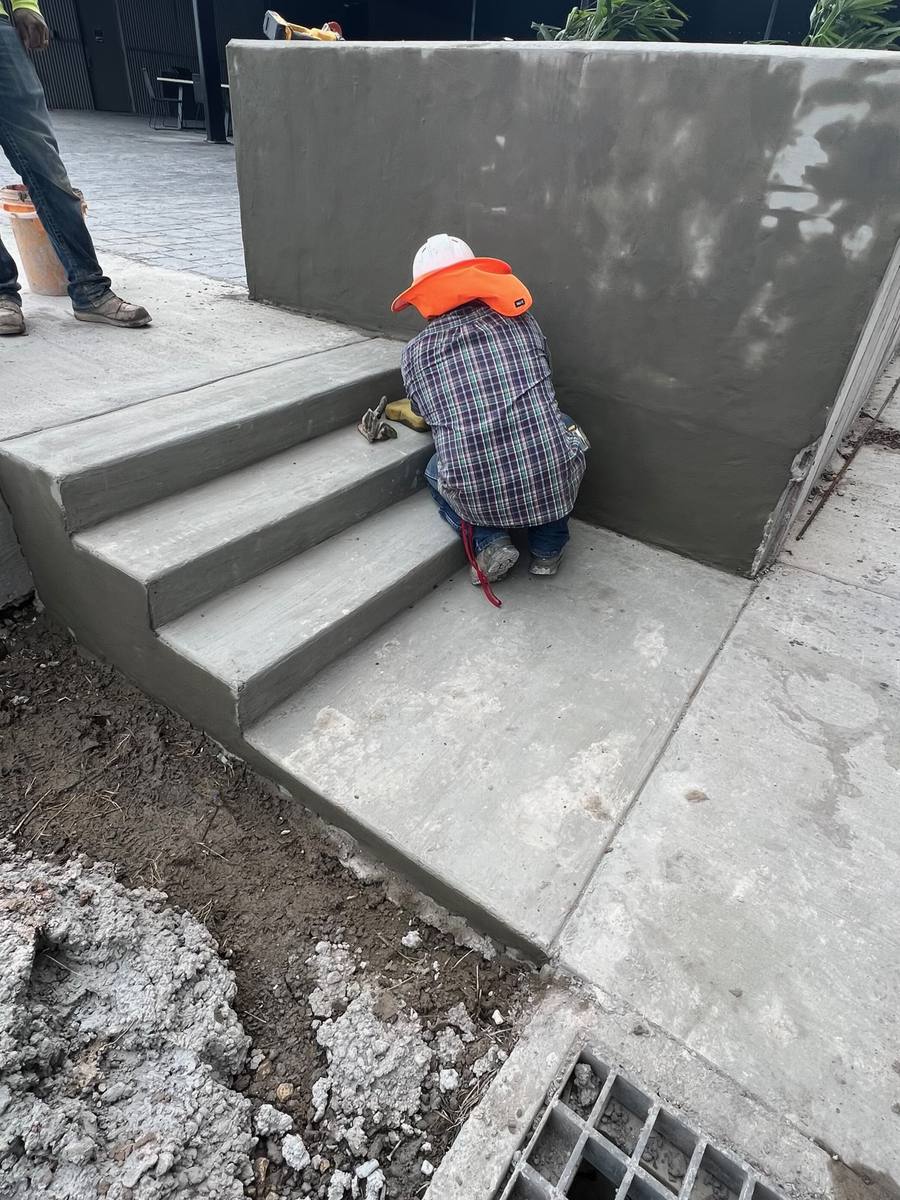 Worker finishing concrete steps beside a retaining wall