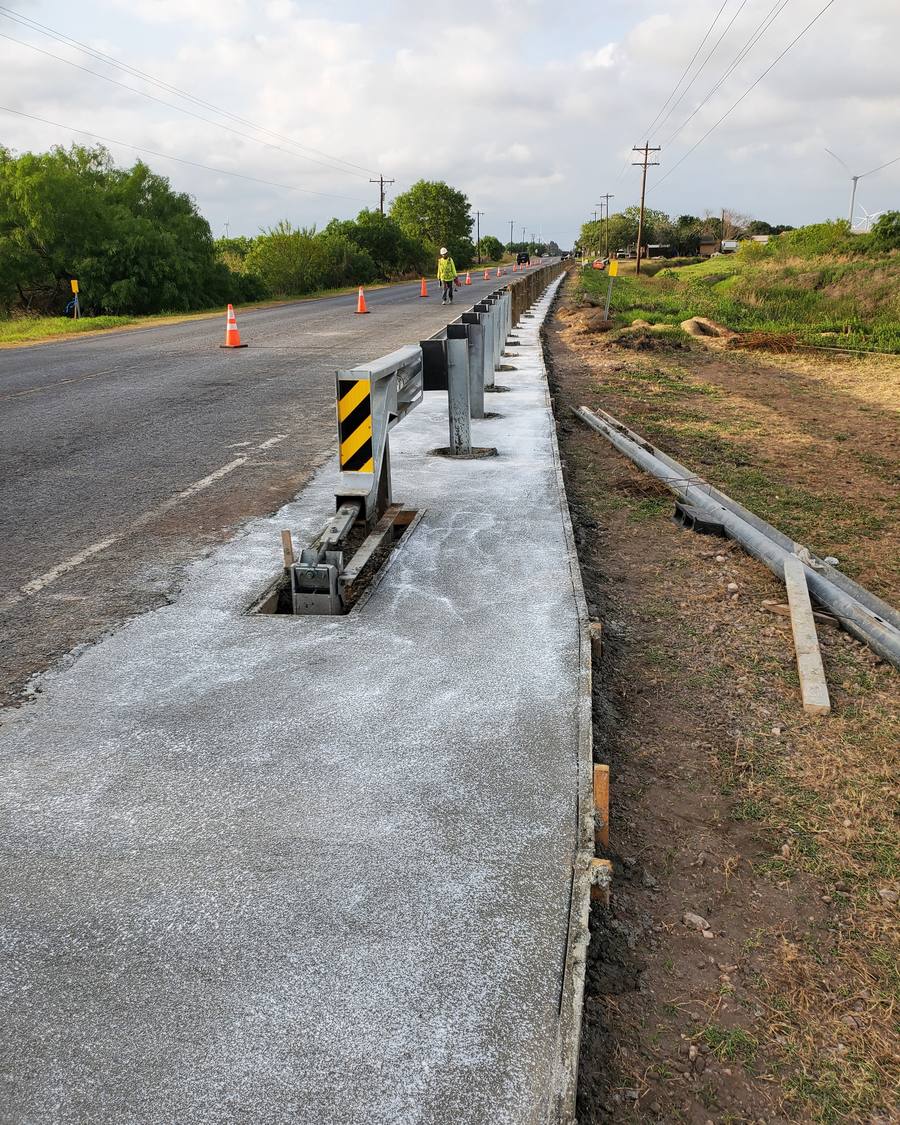 Fresh concrete shoulder beside a roadside guardrail