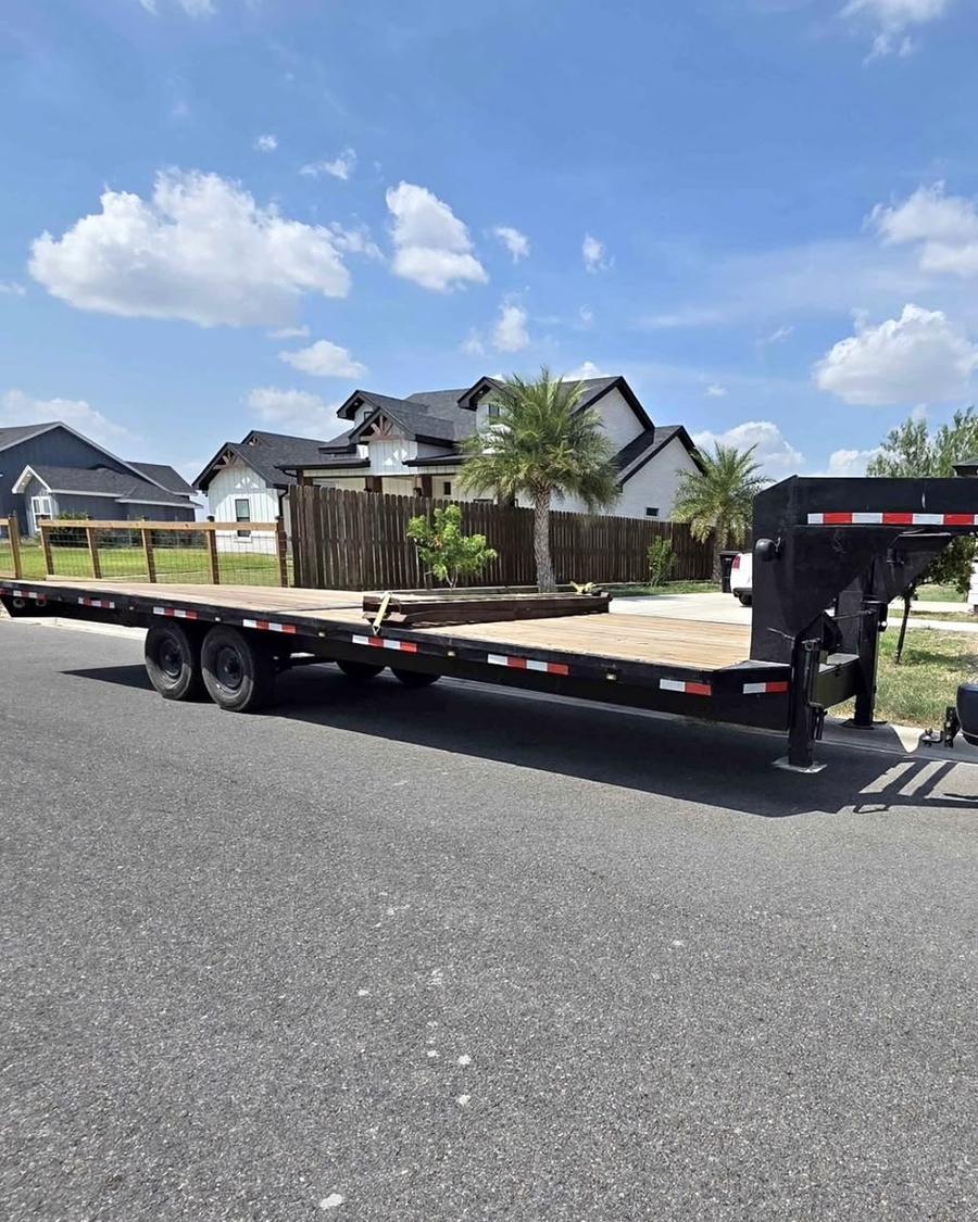 Gooseneck flatbed trailer with a wood deck and tandem axles on a neighborhood street