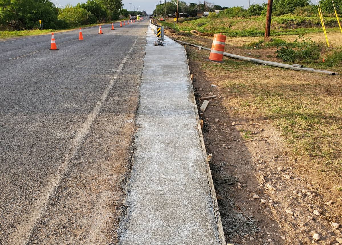 Fresh concrete placed along a roadway beside traffic cones